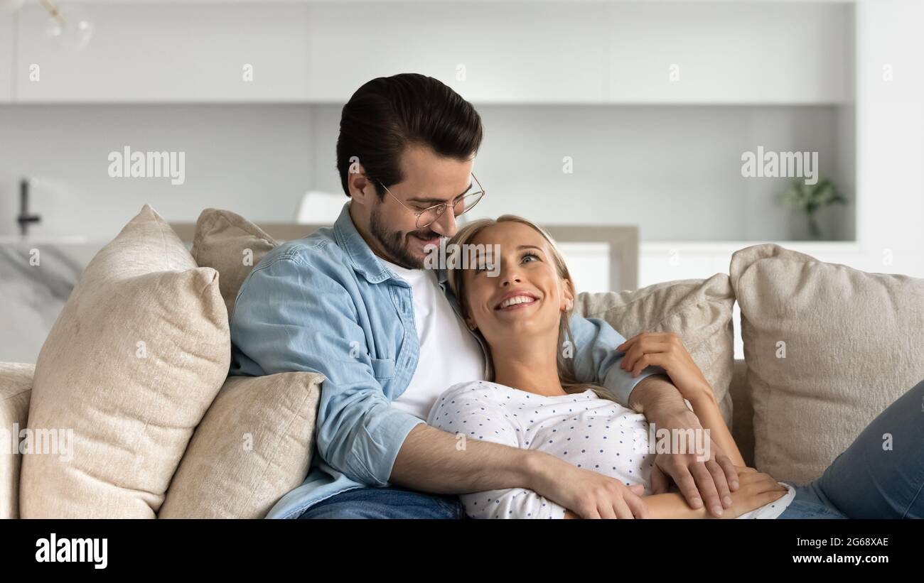 Un jeune couple heureux et marié qui s'embrasse, se détendant sur un canapé confortable ensemble Banque D'Images