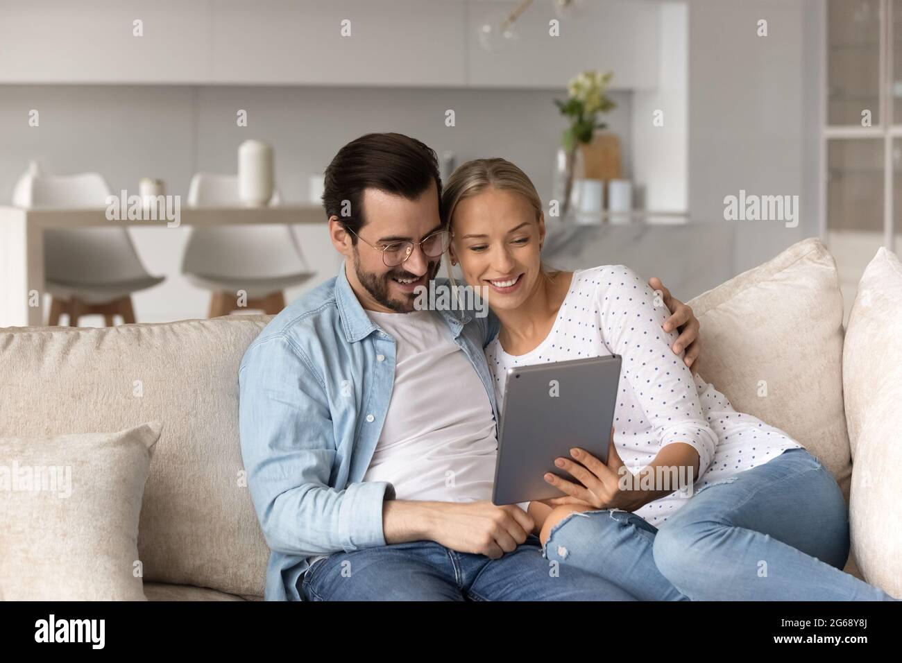 Un jeune couple heureux utilisant une tablette, se détendant sur un canapé ensemble Banque D'Images