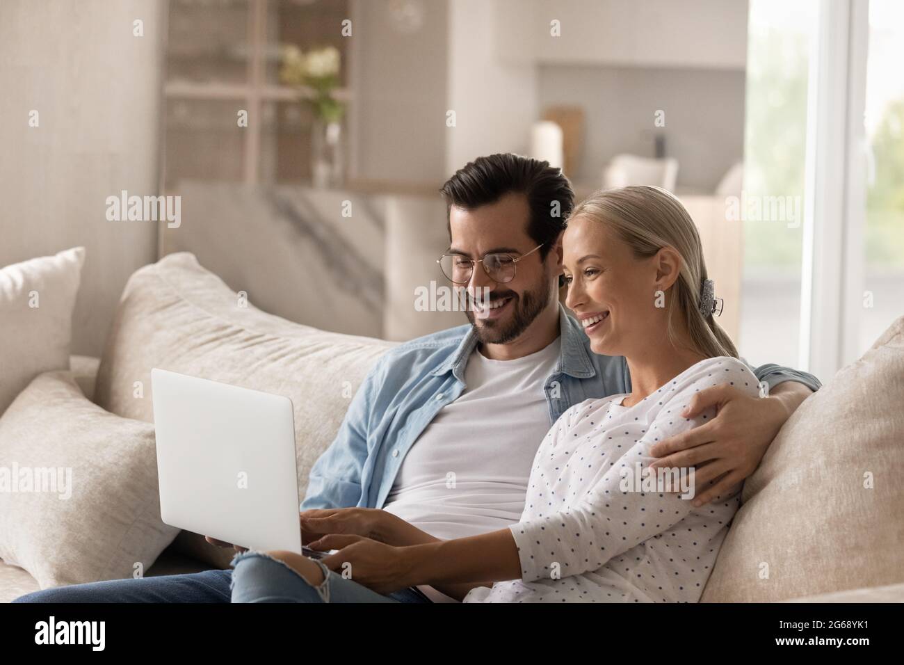 Une femme et un mari heureux se sergeant, se reposant sur un canapé avec un ordinateur portable Banque D'Images