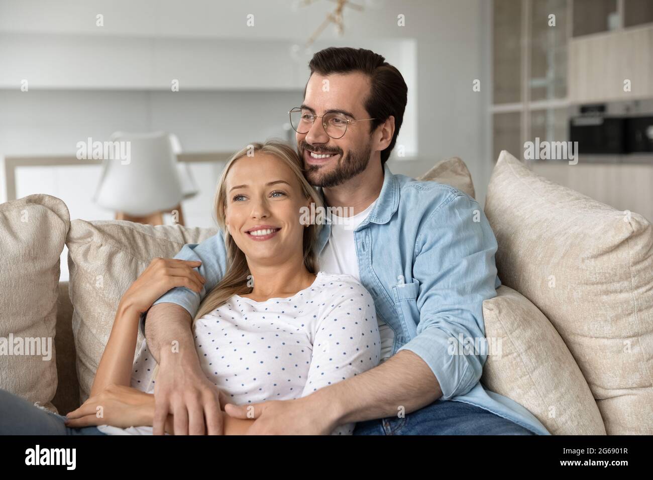 Un jeune couple heureux et rêveur qui s'embrasse, se détendant sur un canapé ensemble Banque D'Images