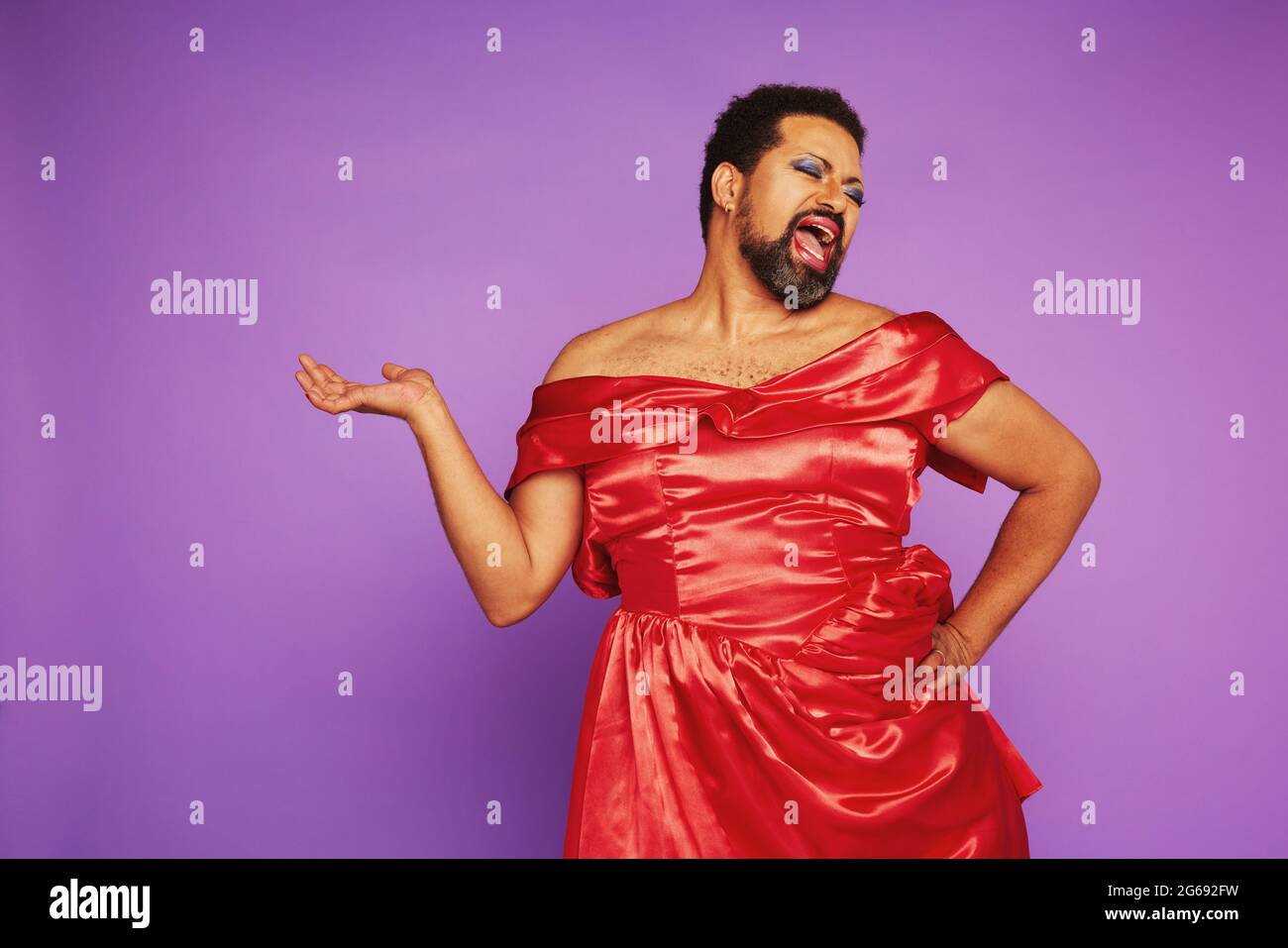 Homme expressif en robe féminine chantant. Glissez la reine portant le maquillage et les femmes s'habillent sur fond violet. Banque D'Images