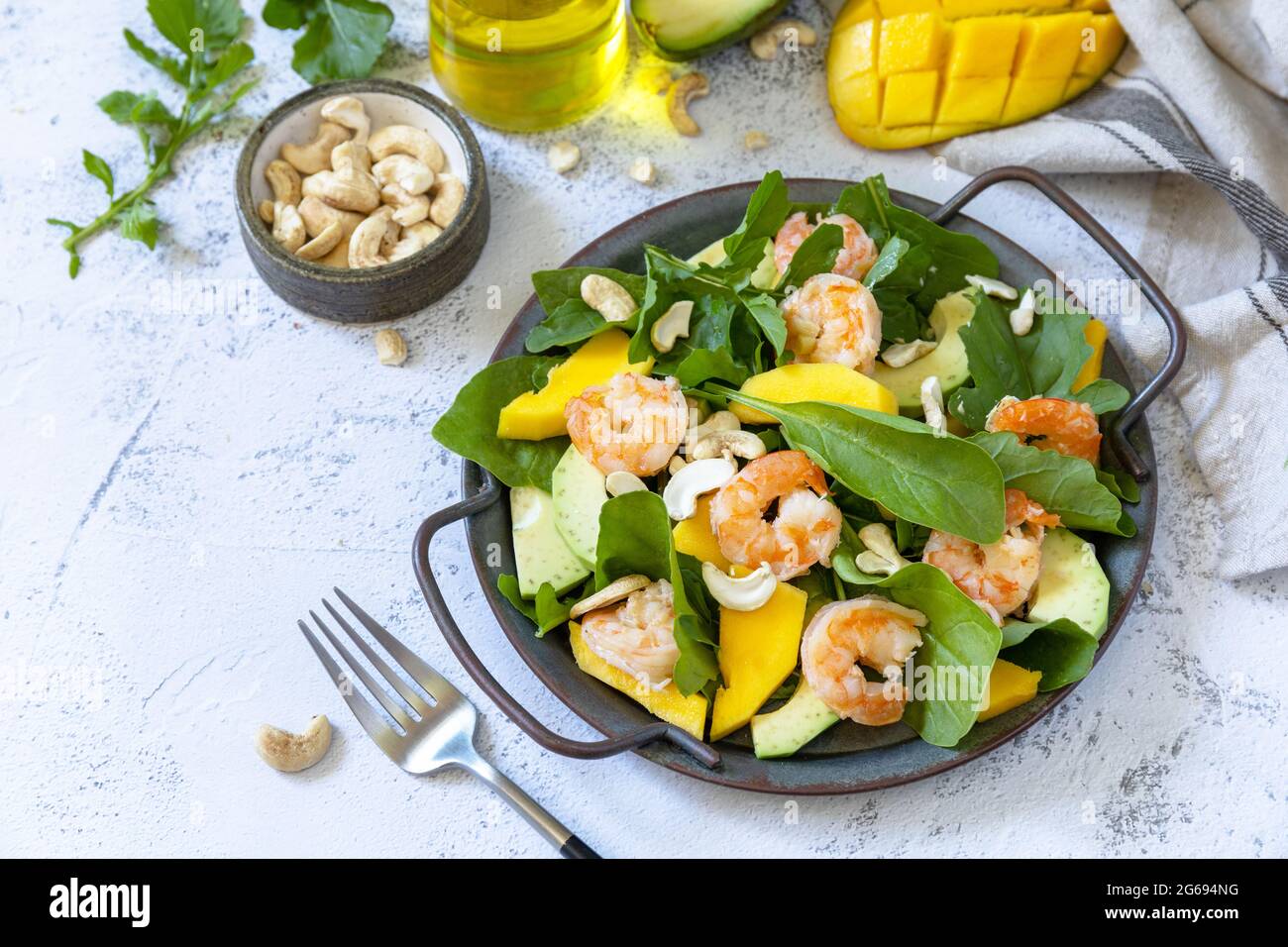 Salade diététique saine avec des arugula, des épinards, de la mangue, de l'avocat, des crevettes, vinaigrette et noix de pécan sur une table en pierre grise. Banque D'Images