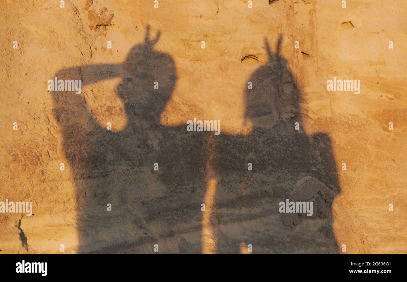 Ombres de deux personnes sur la texture de sable rouge posant avec V ou signes de paix sur leur tête, couple heureux, vacances, vacances d'été ou lune de miel concept Banque D'Images