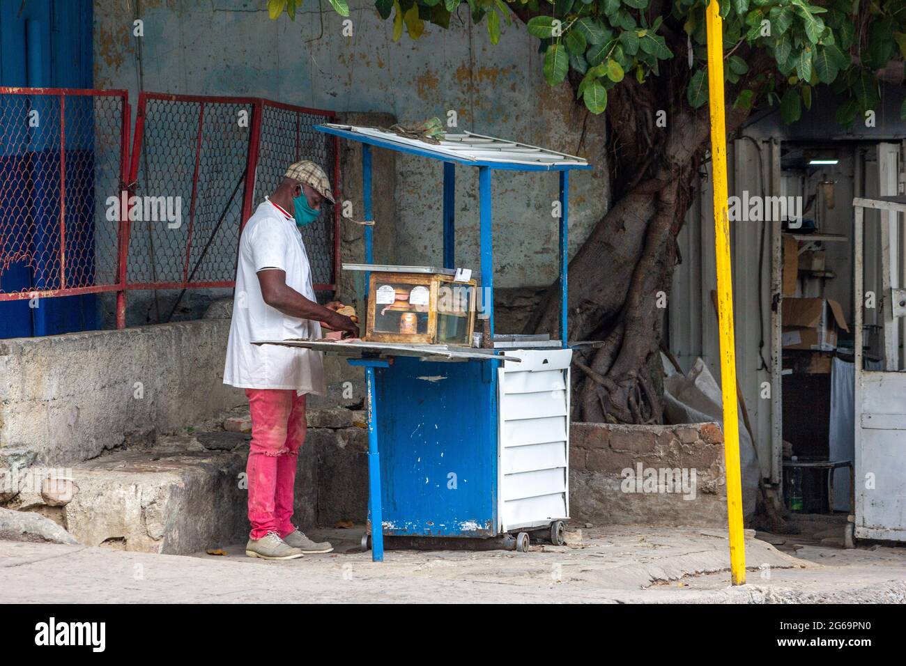 Un homme cubain afro-antillais qui vend des produits alimentaires dans un kiosque situé dans un trottoir de la ville à Santiago de Cuba, Cuba. Il porte un masque de protection Banque D'Images