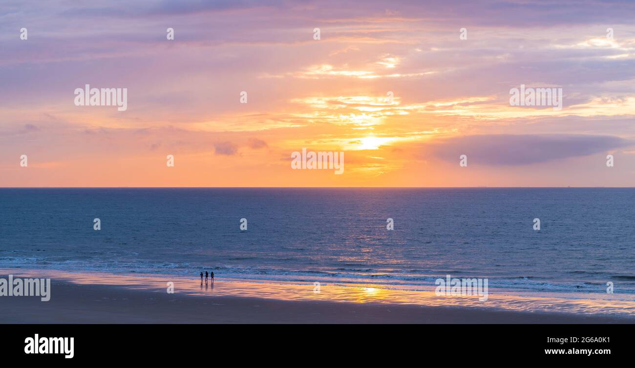 Trois personnes profitant d'un coucher de soleil sur la plage de la mer du Nord, Oostende (Ostende), Belgique. Banque D'Images
