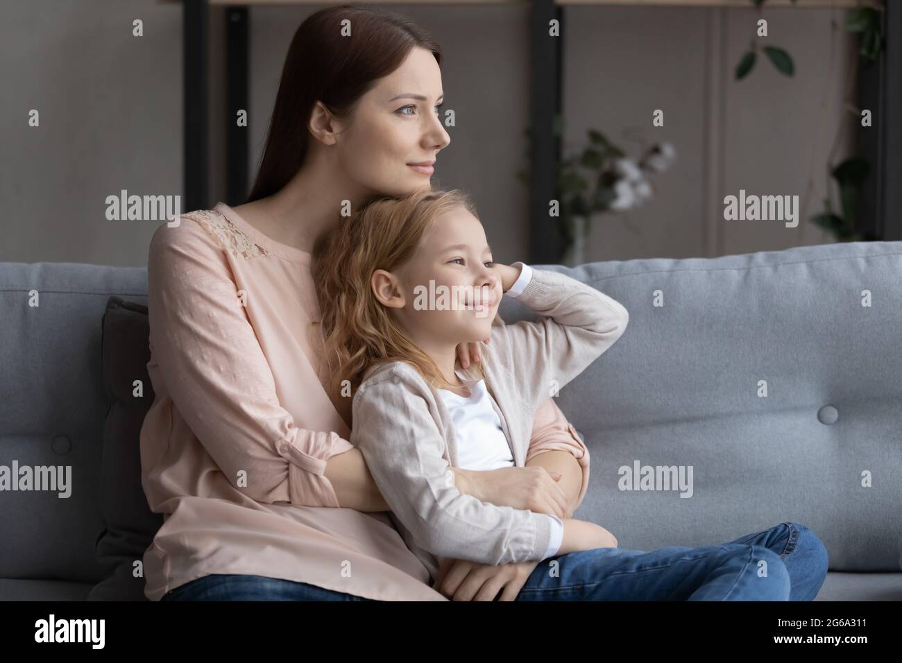Une jeune fille aux cheveux rouges souriants se penche vers la mère sur le canapé Banque D'Images