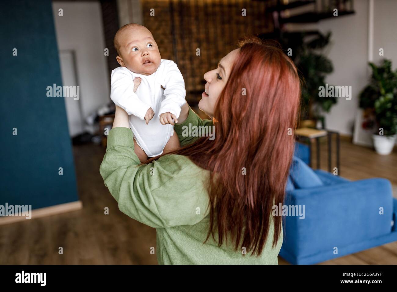 Joyeux jeune caucasien rouge a poil de la mère de soulever bébé mignon fils, jouant avec le bébé biracial afro-américain garçon à la maison. Race mixte maman et petit Banque D'Images