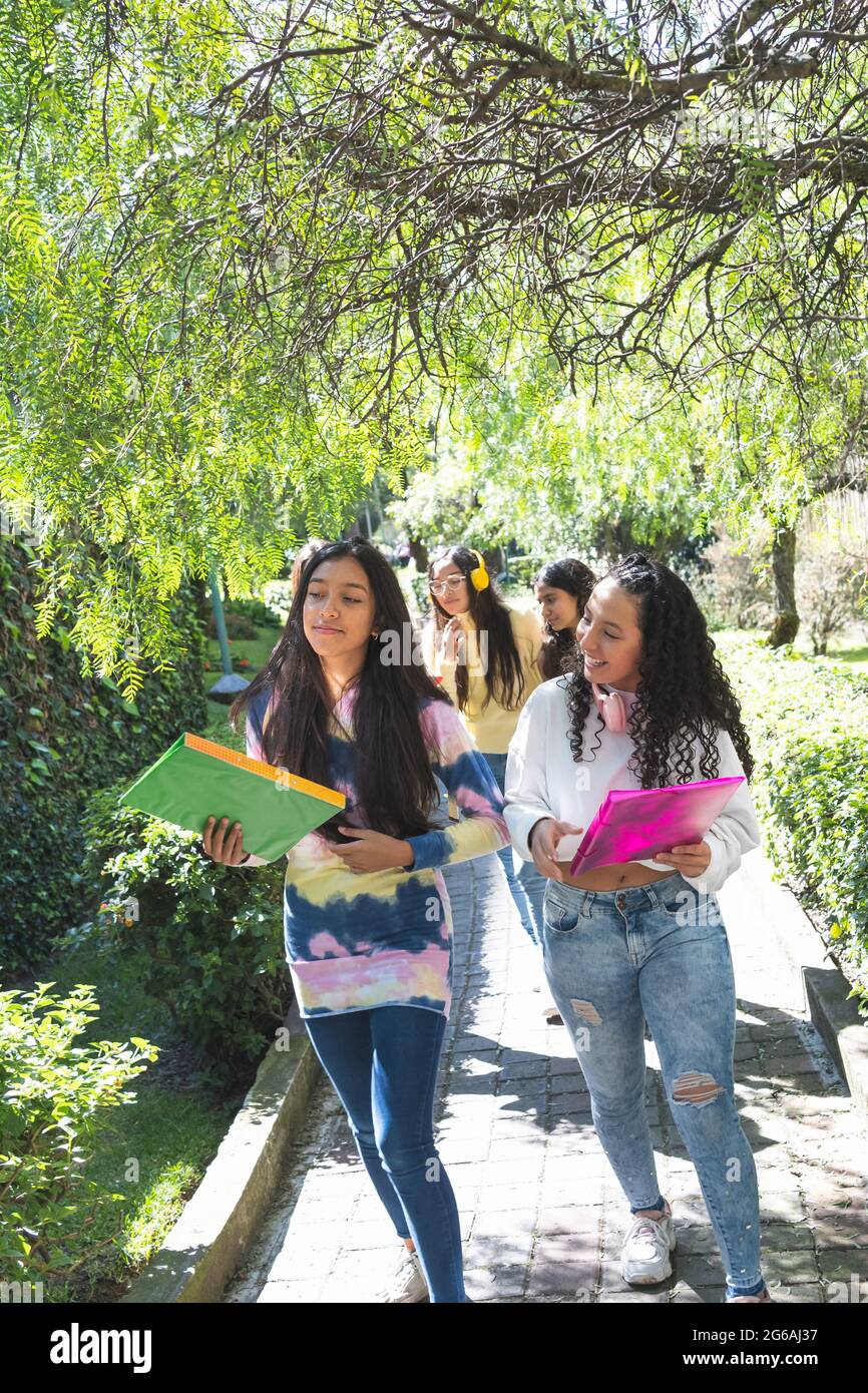 Attention sélective de deux adolescents Latina amis se dirigeant heureusement à l'école secondaire avec d'autres amis derrière eux un matin ensoleillé. Concept d'éducation Banque D'Images