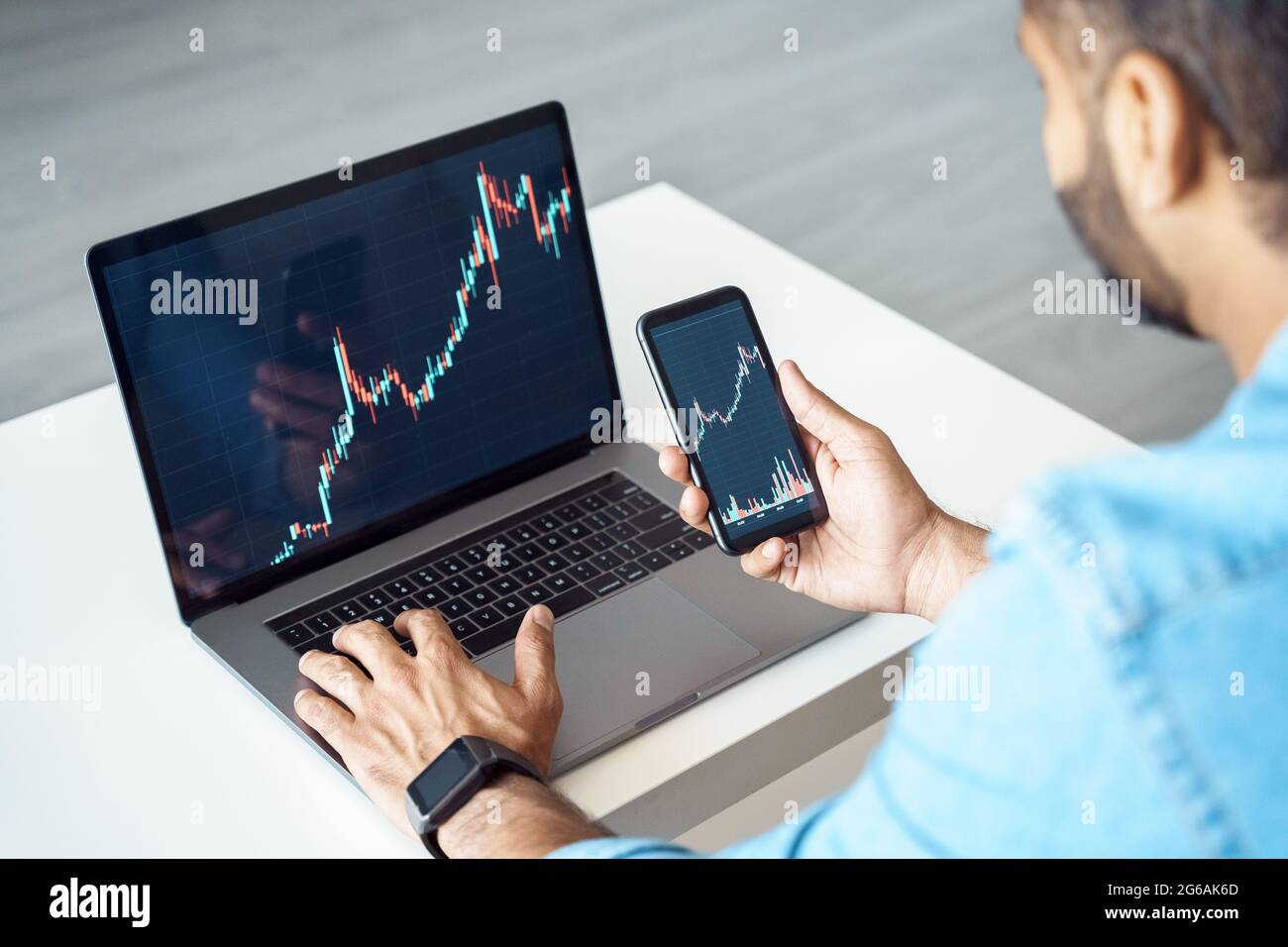 Homme d'affaires Trader investisseur analyste utilisant l'application de téléphone mobile et ordinateur portable vue arrière Banque D'Images