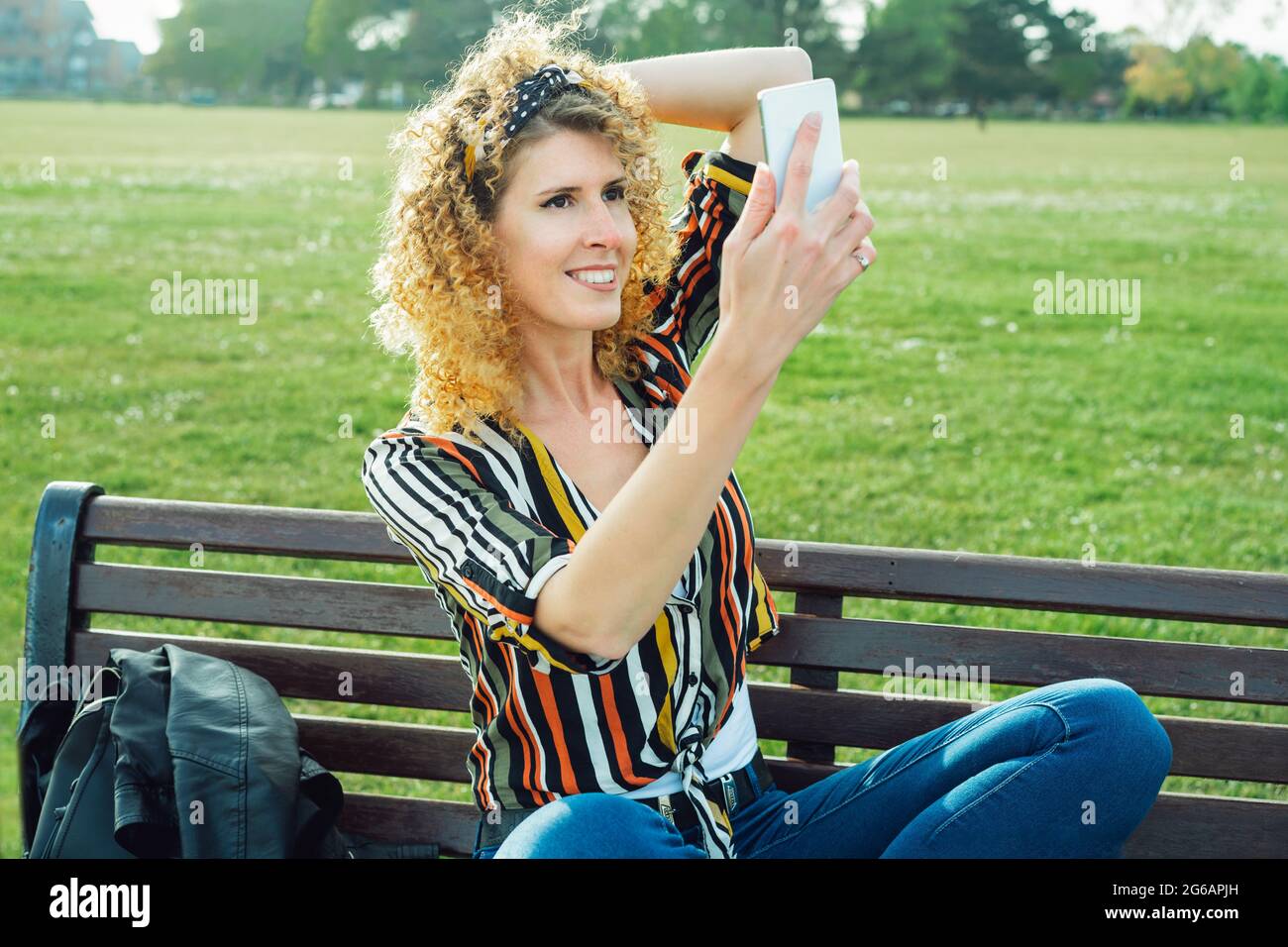 Une femme qui fait des photos de selfie sur un téléphone portable. Élégante femme souriante en chemise multicolore à rayures, posant sur le fond de la loi verte Banque D'Images