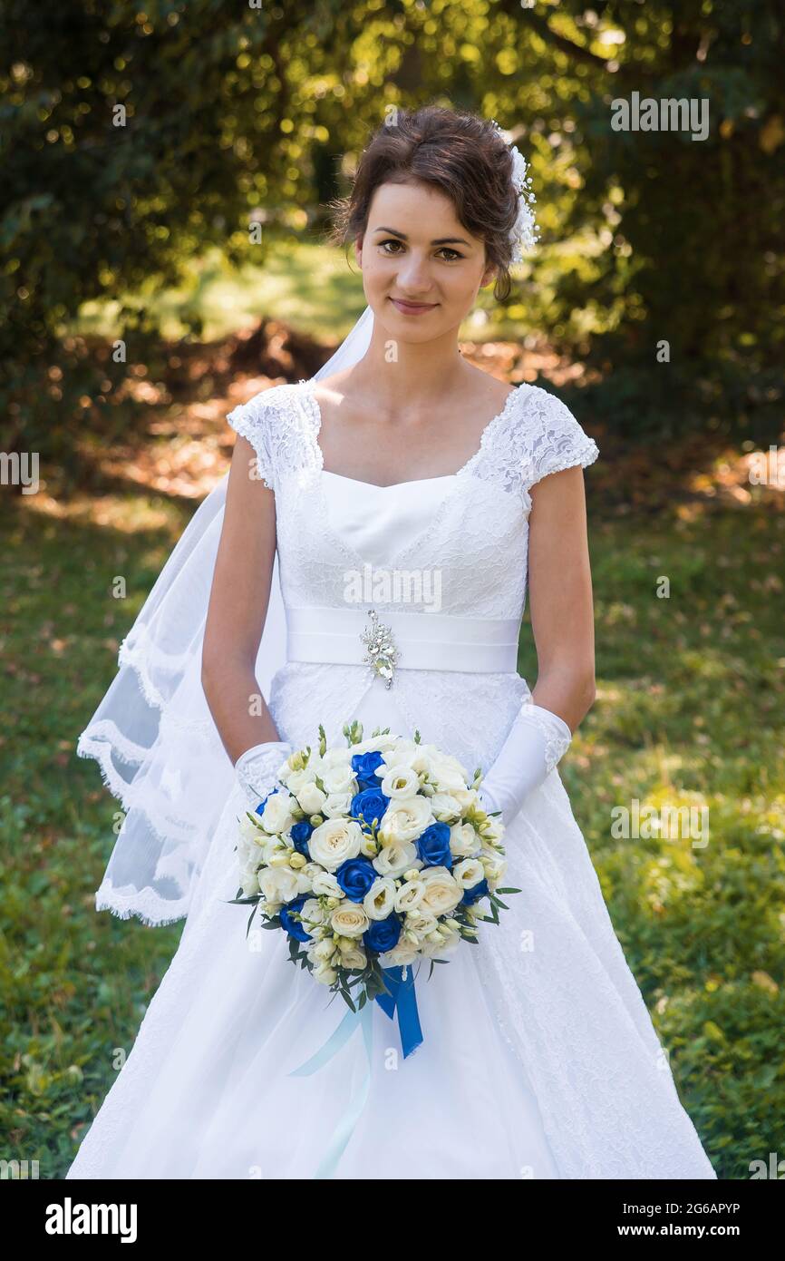 Biélorussie, région de Minsk - 11 août 2018 : jeune mariée brune d'apparence européenne dans une robe de mariage blanche contient un bouquet de lumière et de bleu f Banque D'Images