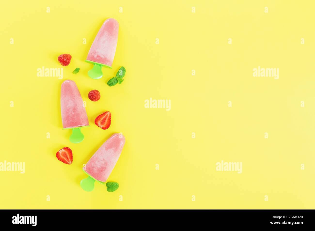 Flat Lay avec une crème glacée au sorbet congelé rose fruité sur un bâton en plastique vert collection avec des coupes de fraise, des feuilles de menthe sur fond jaune. Gelé Banque D'Images