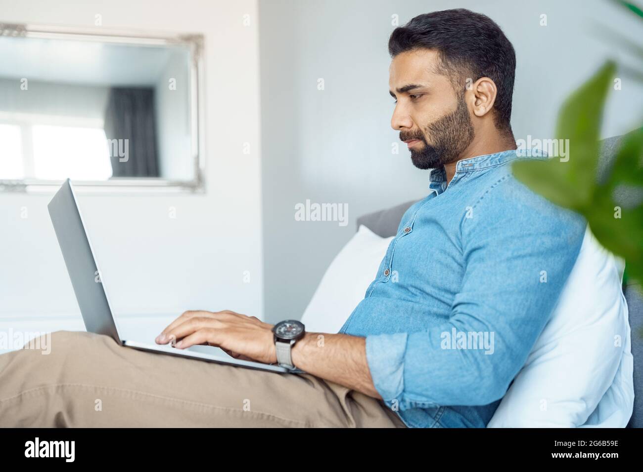 Un homme d'affaires indien sérieux travaillant sur un ordinateur portable, assis sur le lit de la maison Banque D'Images