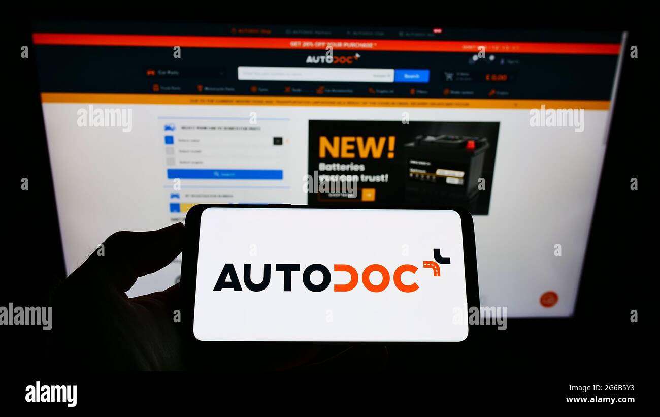 Personne tenant un smartphone avec le logo du détaillant allemand de pièces  de rechange automobile Autodoc GmbH en ligne sur l'écran devant le site  Web. Mise au point sur l'affichage du téléphone
