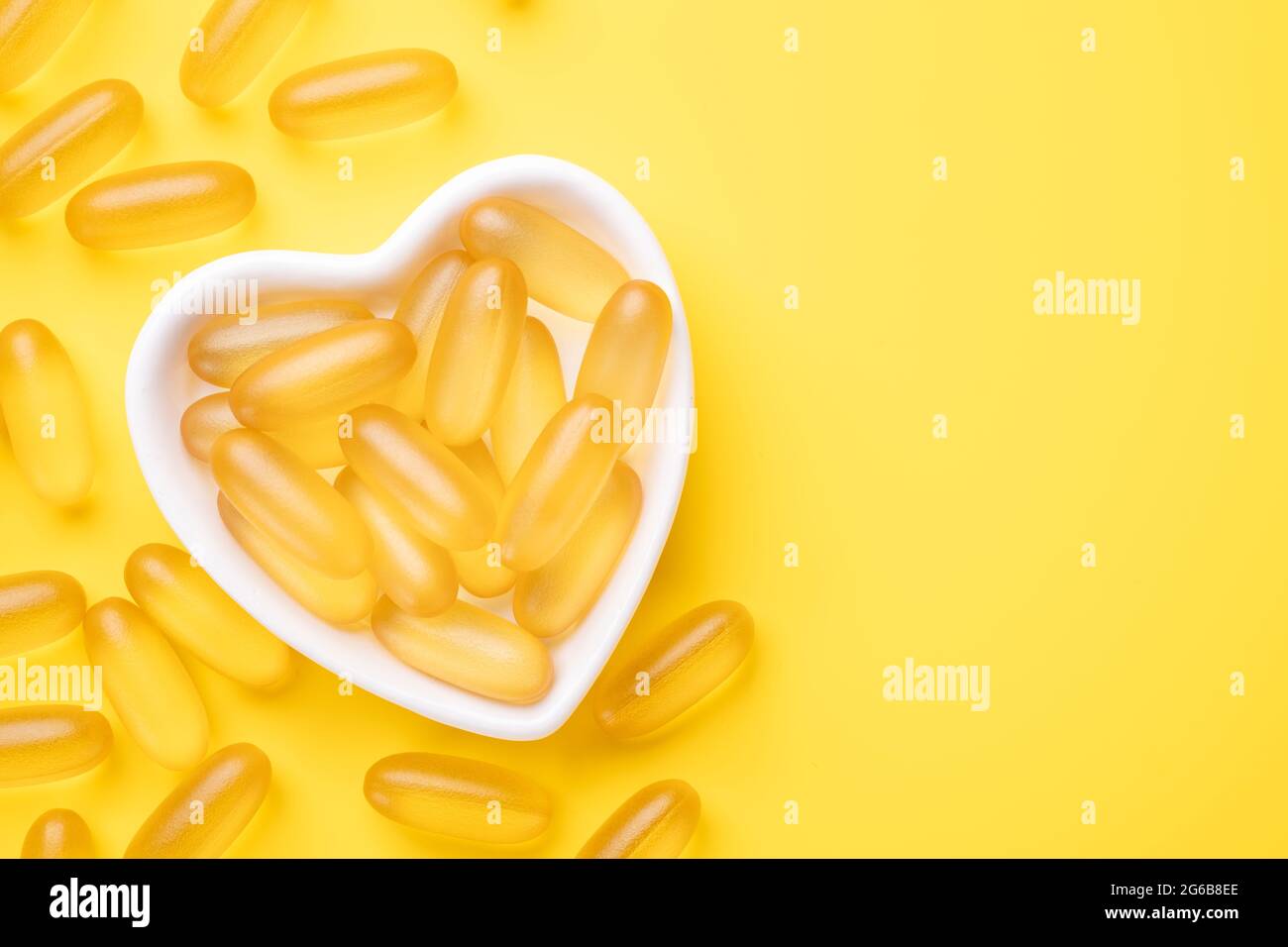 Les capsules d'huile de poisson de vitamine D et Omega 3 complètent dans une plaque en forme de cœur sur fond jaune. Concept de soins de santé. Vue de dessus - image Banque D'Images