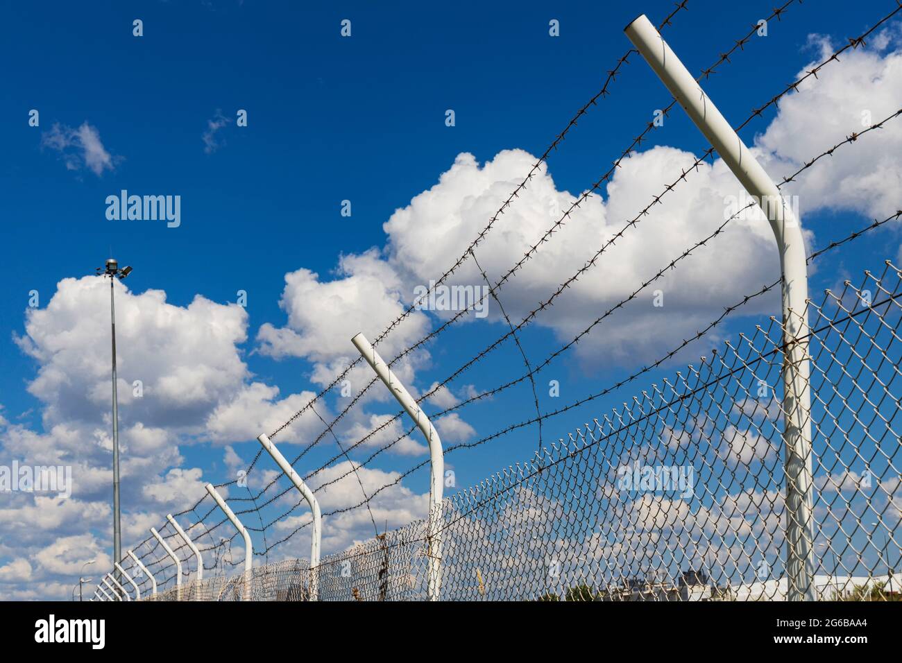 Haut d'une clôture en métal avec des lignes de fil de rasoir sur le fond d'un ciel bleu avec des nuages Banque D'Images