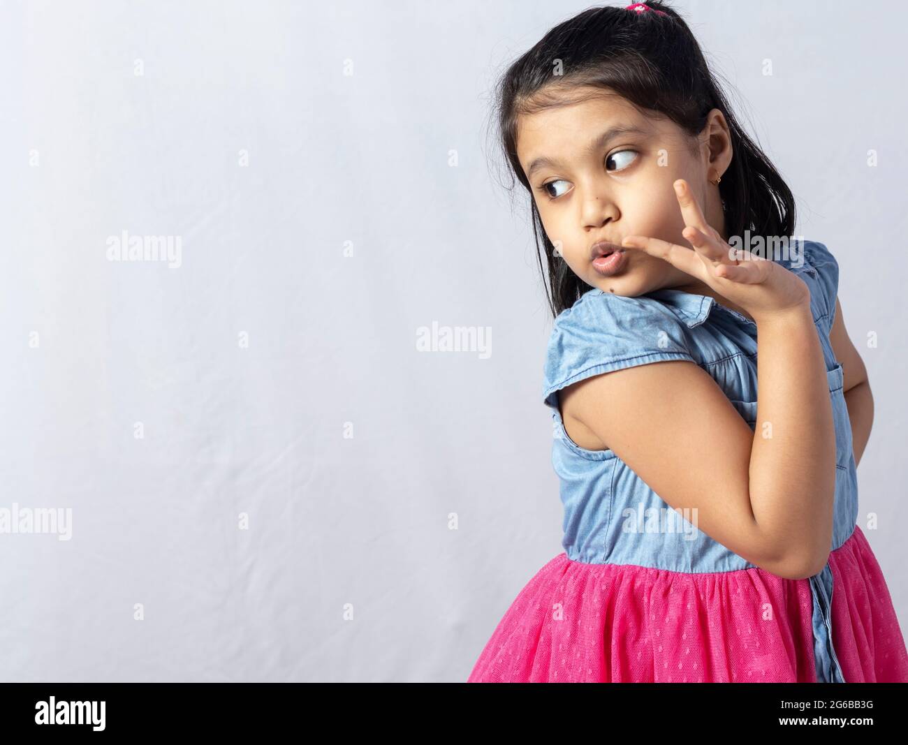 Une jolie petite fille indienne mignonne à la recherche de son côté droit avec un visage surpris isolé sur fond blanc Banque D'Images