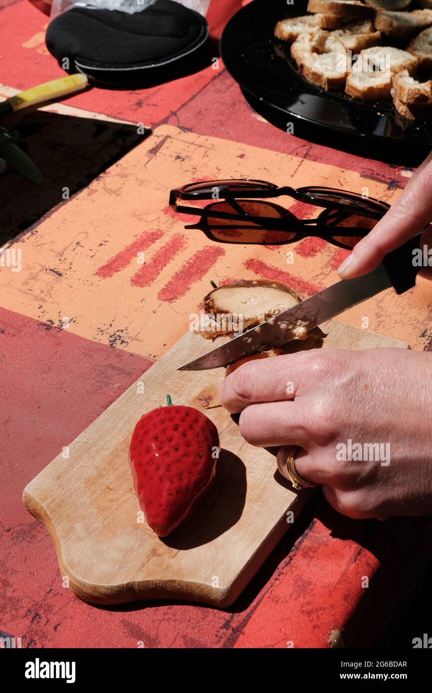 Gros plan d'une femme qui coupe un bloc de foie gras sur une planche à découper et une fraise Banque D'Images