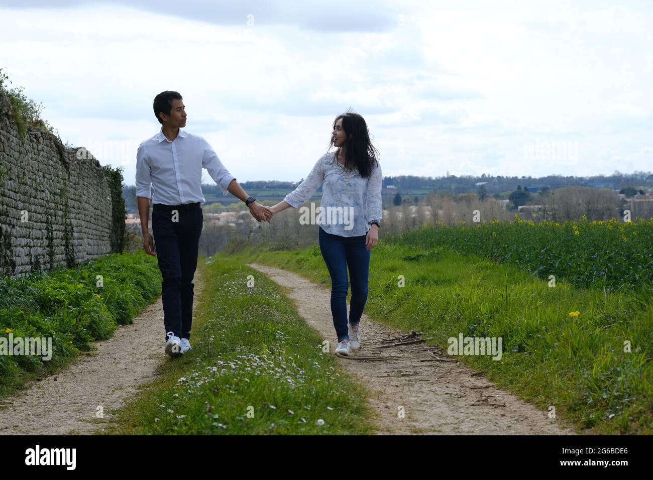 Heureux couple marchant le long d'une route de campagne tenant les mains, France Banque D'Images