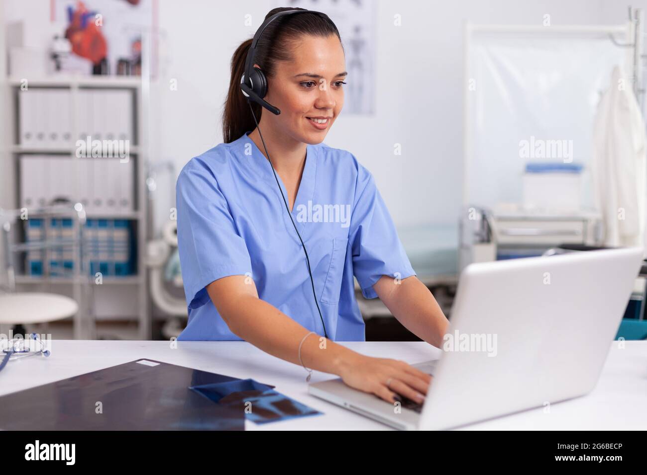 Réceptionniste médicale portant un micro-casque dans un hôpital privé  dactylographiant sur un ordinateur portable médecin de santé assis au  bureau à l'aide d'un ordinateur dans une clinique moderne regardant le  moniteur Photo