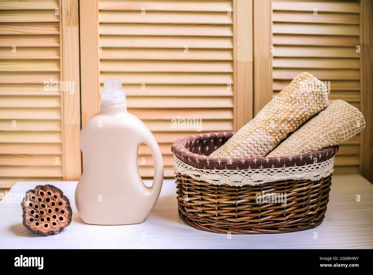 Gel pour laver le linge dans une bouteille en plastique près d'une pile de serviettes propres dans le panier. Composition sur étagère en bois blanc sur fond en bois. Banque D'Images