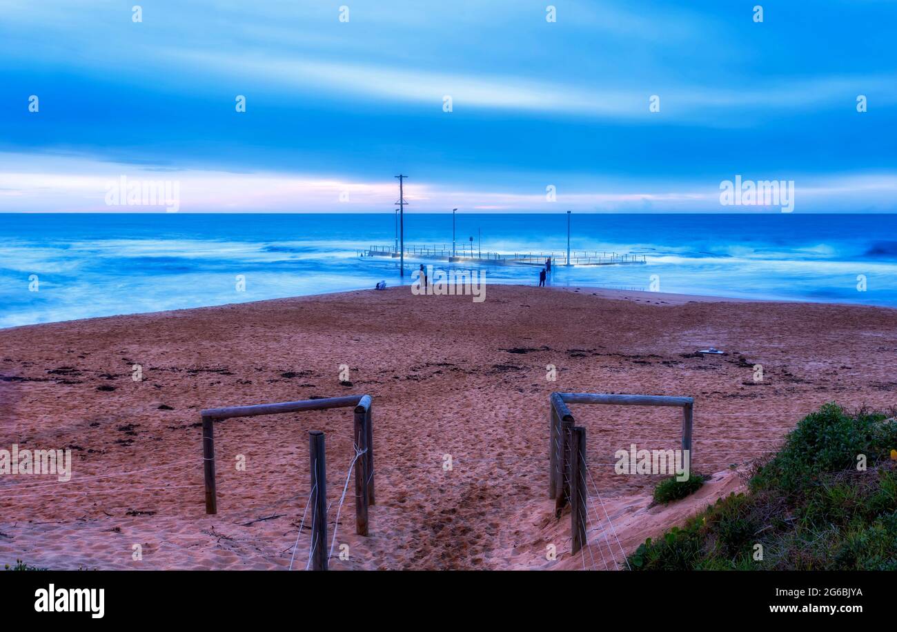 Entrée à la plage de sable de Mona Vale à marée haute avec piscine de roche coupée au large de la rive - paysage marin pittoresque au lever du soleil. Banque D'Images