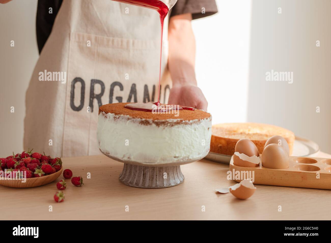 Male pastry chef pouring confiture ou sirop dans morceau de gâteau délicieux sur table en bois Banque D'Images