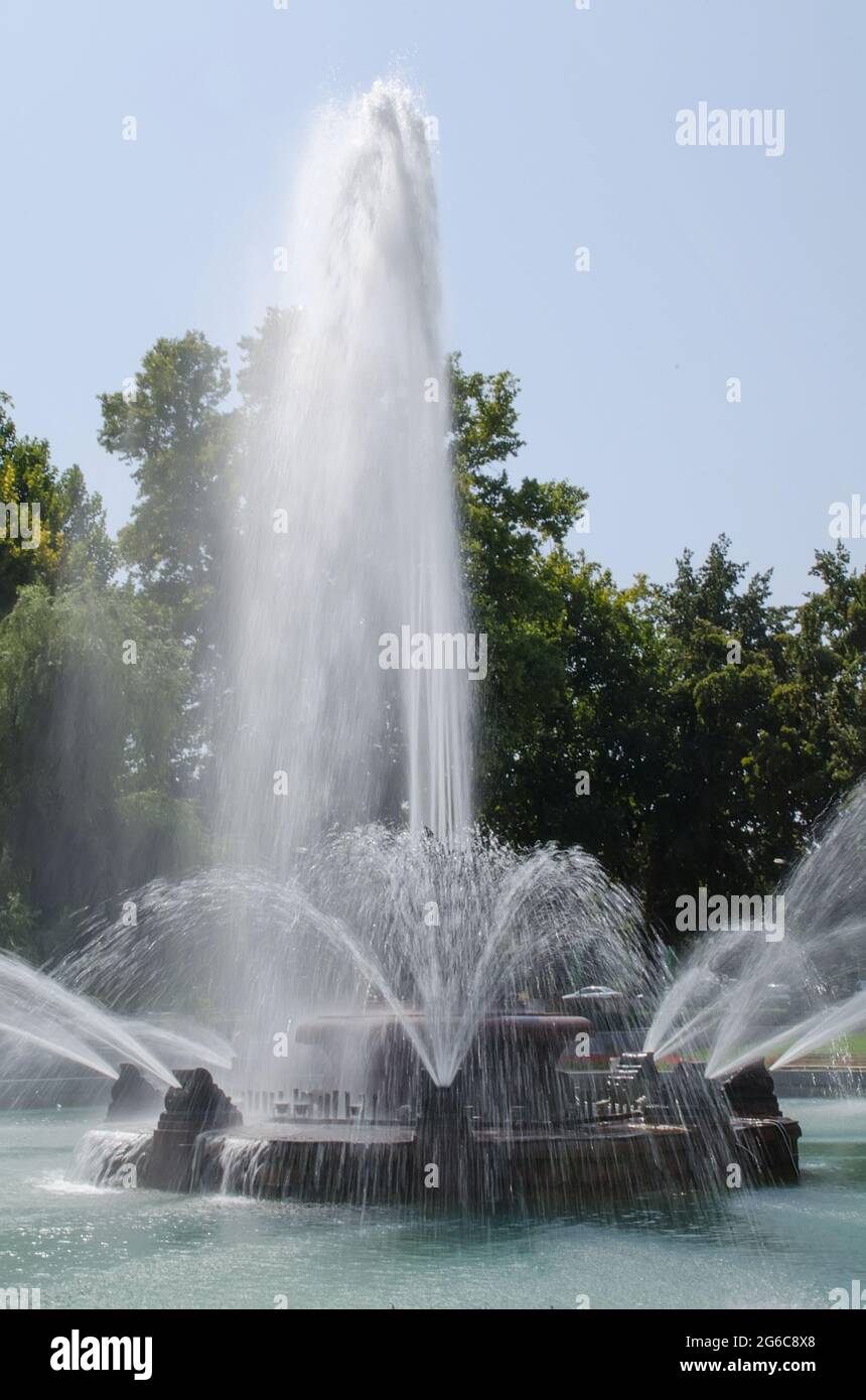Grande fontaine dans le parc à l'intérieur d'une piscine d'eau en face des arbres verts et du ciel bleu Banque D'Images