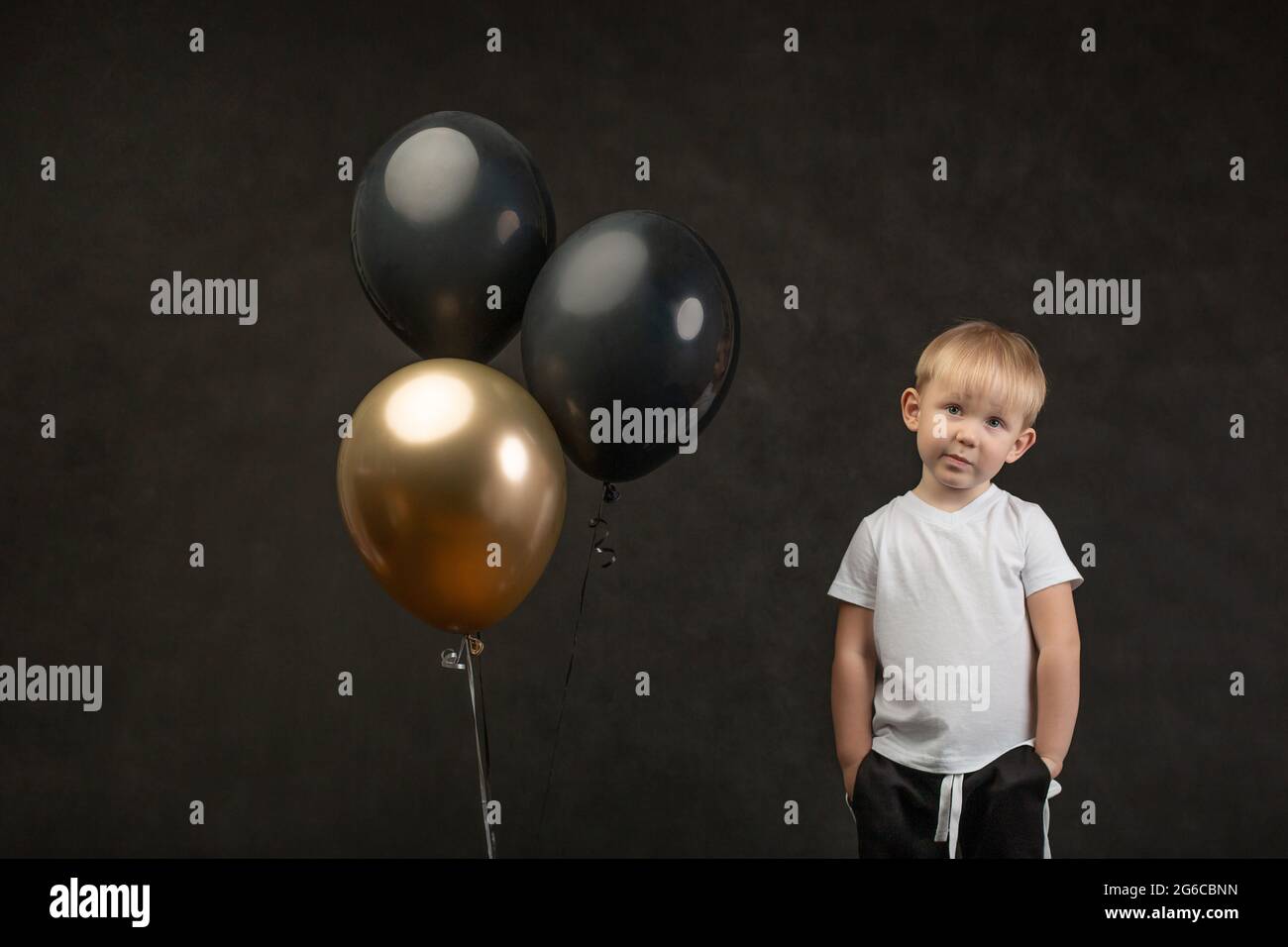 Enfant enfant très petit 3 ans, déçu, sceptique, avec des ballons regardant dans l'appareil photo sur fond noir. Concept pour carte d'anniversaire et solde noir Banque D'Images