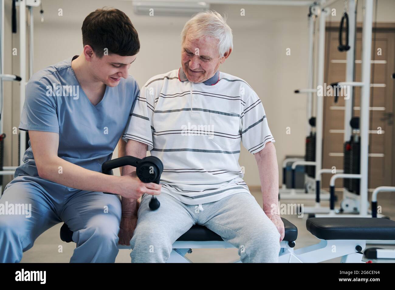 Physiothérapeute offrant un traitement des jambes à un citoyen âgé avec un pistolet de massage Banque D'Images