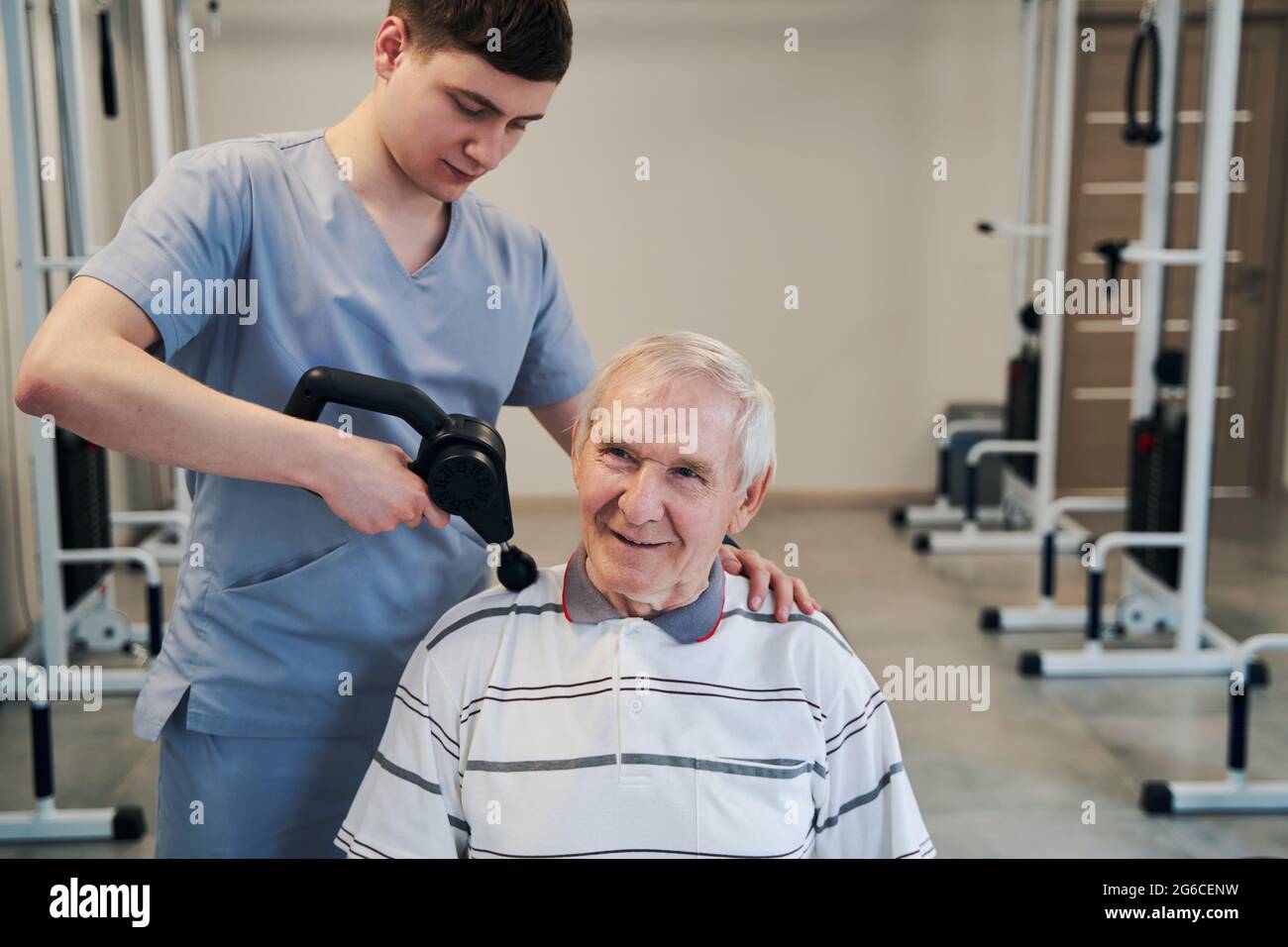 Orthopédiste utilisant un masseur à percussion sur une épaule mâle âgée Banque D'Images