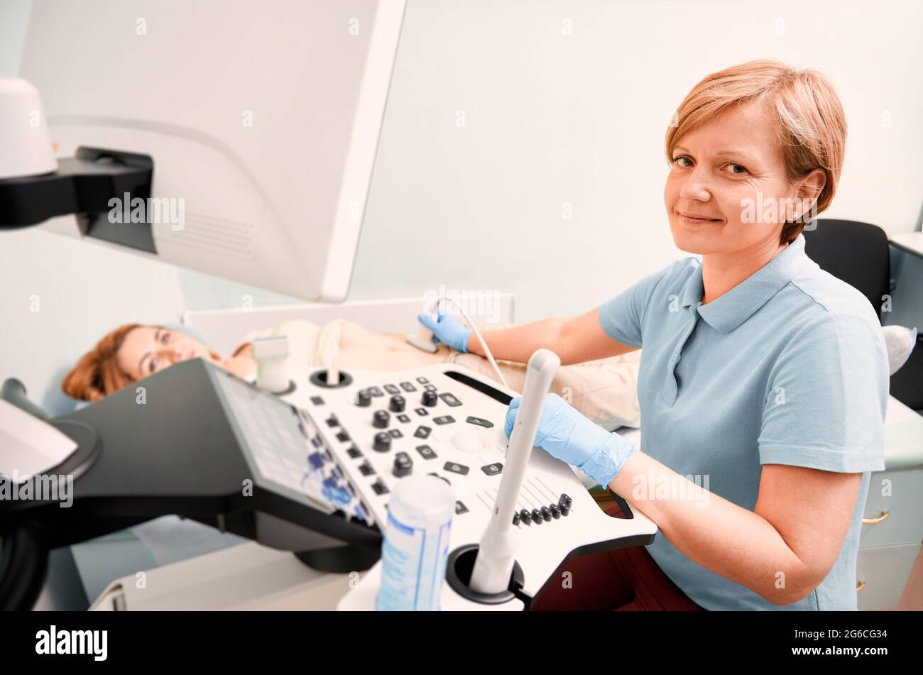 Échographiste en gants stériles examinant une patiente avec un échographe. Femme médecin regardant l'appareil photo et souriant pendant l'examen échographique. Concept de diagnostic échographique. Banque D'Images