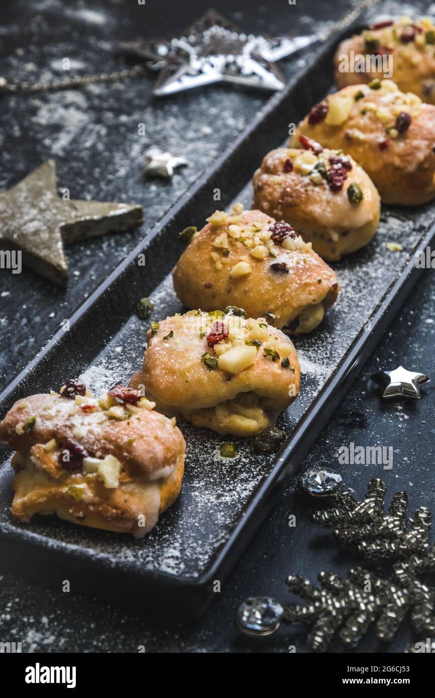 Mini-stollen maison avec glaçage, canneberges séchées et pistaches sur un plateau noir sur fond noir, décoré d'étoiles argentées. Brut vertical Banque D'Images