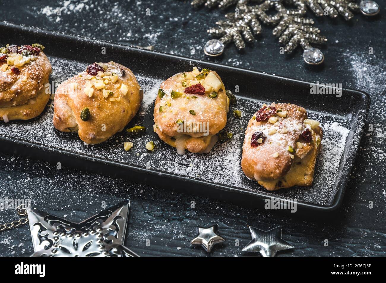 Mini-stollen maison avec glaçage, canneberges séchées et pistaches sur un plateau noir sur fond noir, décoré d'étoiles argentées. Banque D'Images