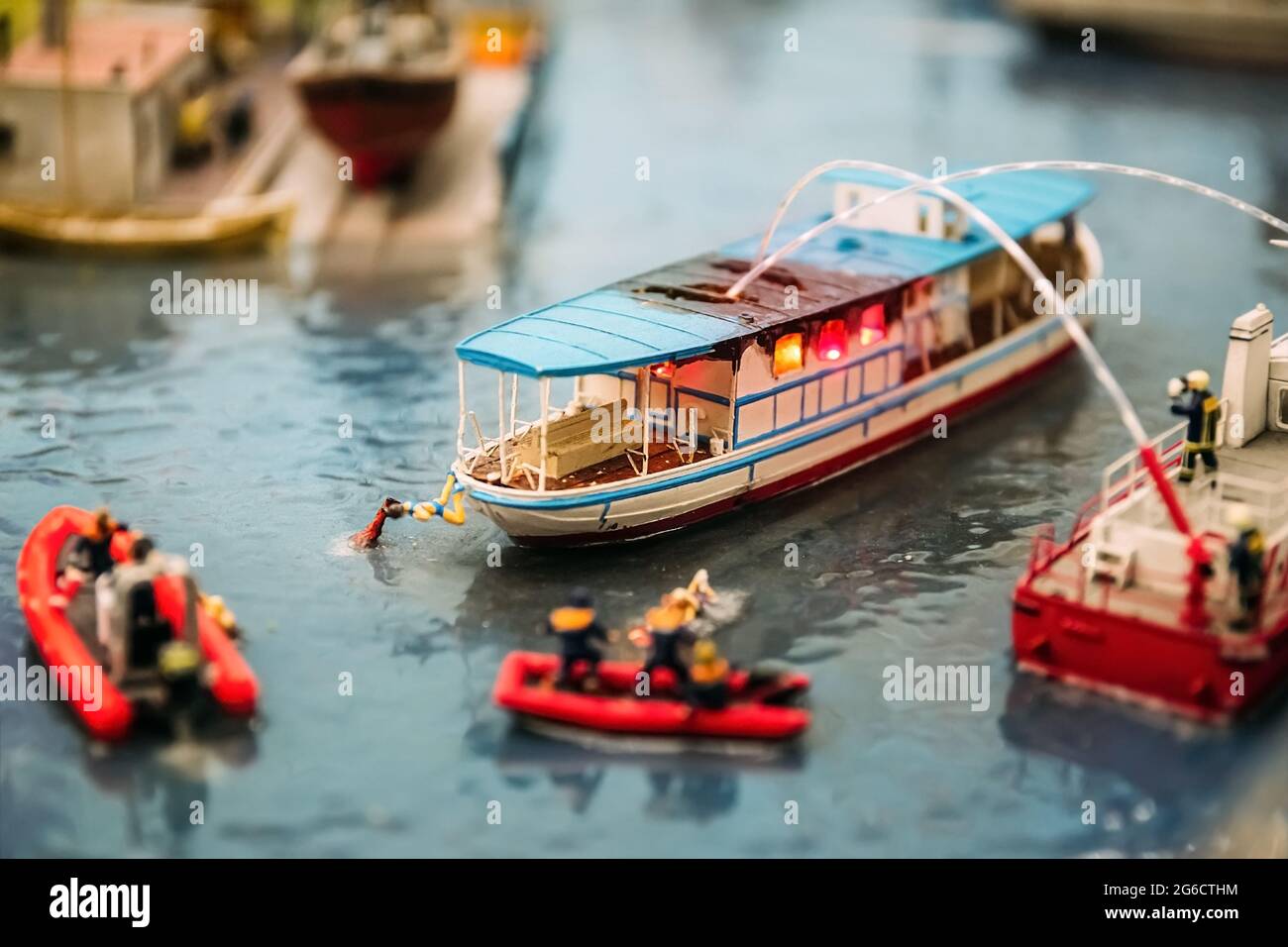 Personnes miniatures. Des modèles miniatures de pompiers éteignent un feu sur un bateau sur l'eau. Modèles miniatures comme un passe-temps. Maquette. Banque D'Images