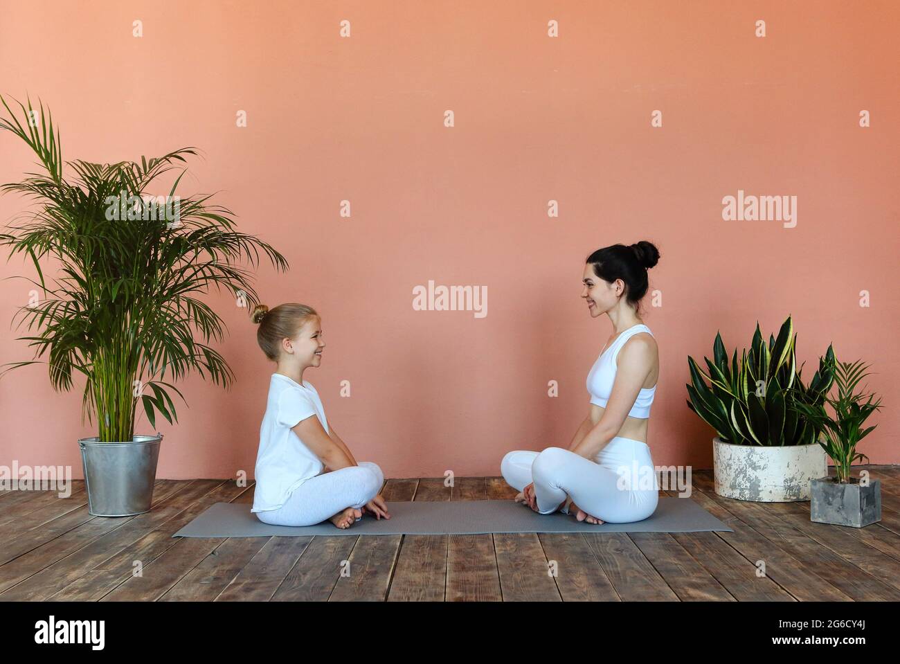 Vue latérale d'une femme souriante et d'une petite fille pratiquant la pose de yoga tout en piquant sur le tapis dans le salon confortable et en regardant loin Banque D'Images