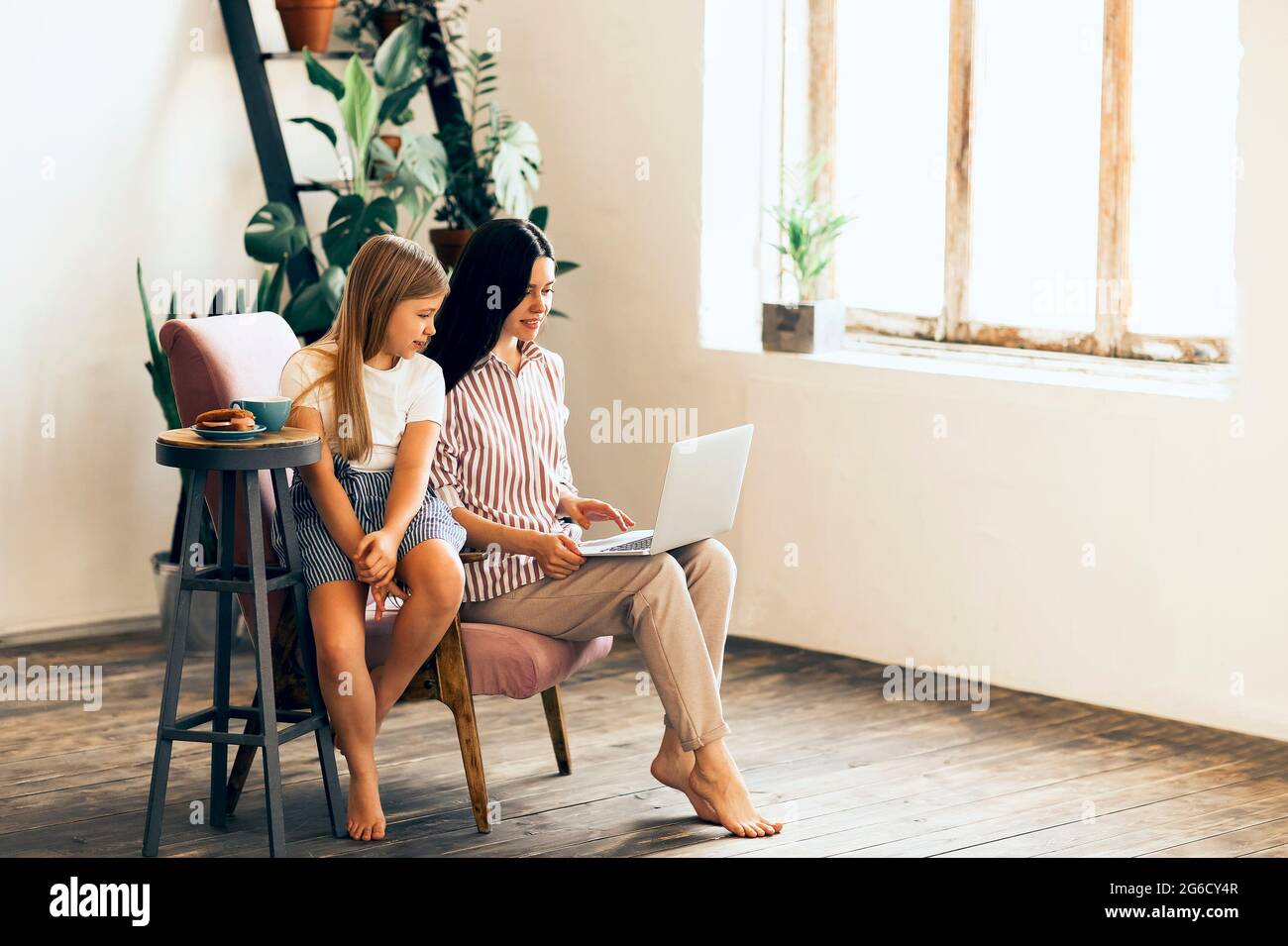 Adorable fille embrassant une jeune femme travaillant sur un ordinateur portable dans un salon confortable Banque D'Images