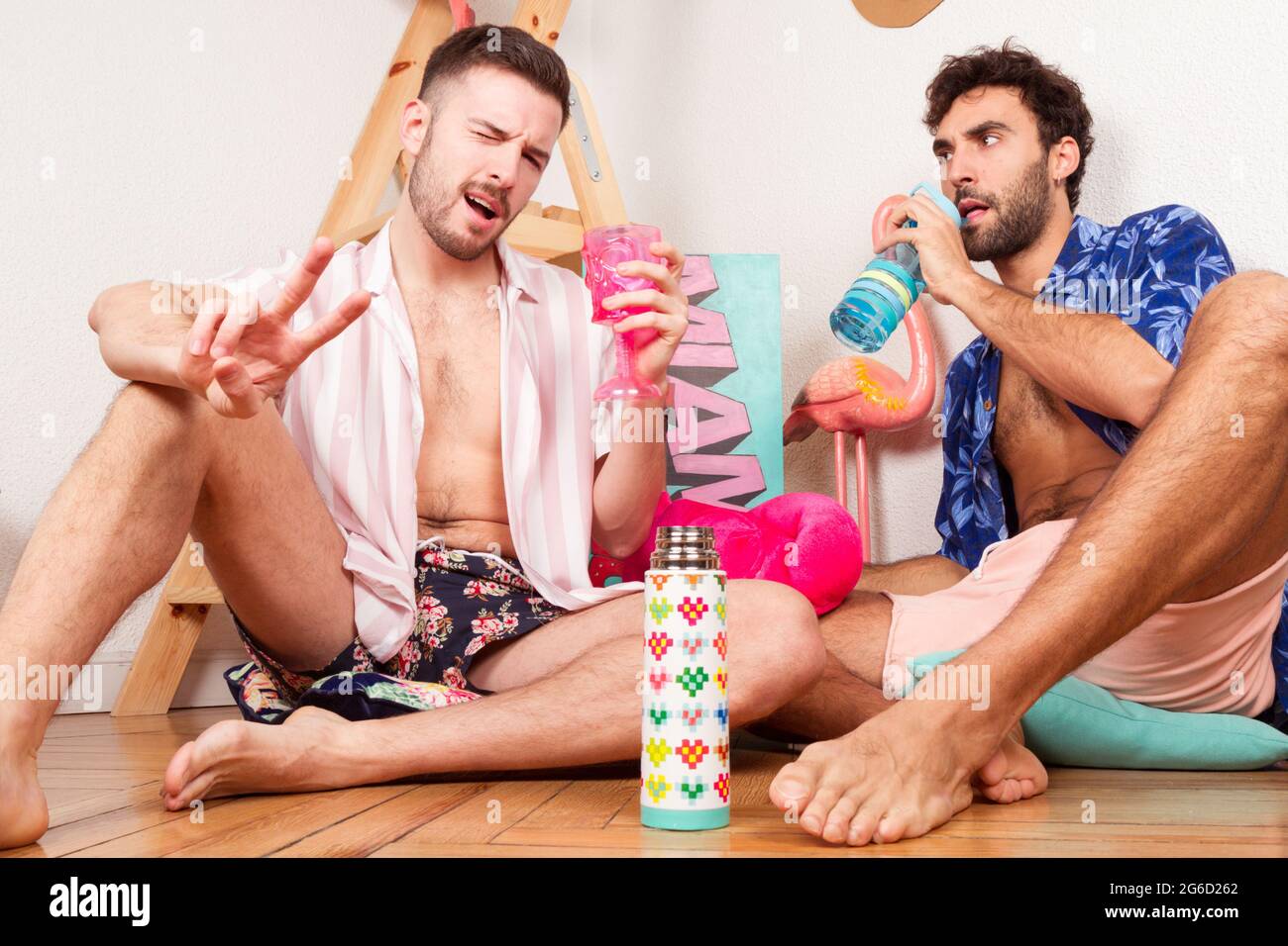 Drôle excités divers adultes homosexuels boyamis dans les tenues d'été avec des boissons prétendant être sur la plage avec flamants roses et s'amuser ensemble Banque D'Images