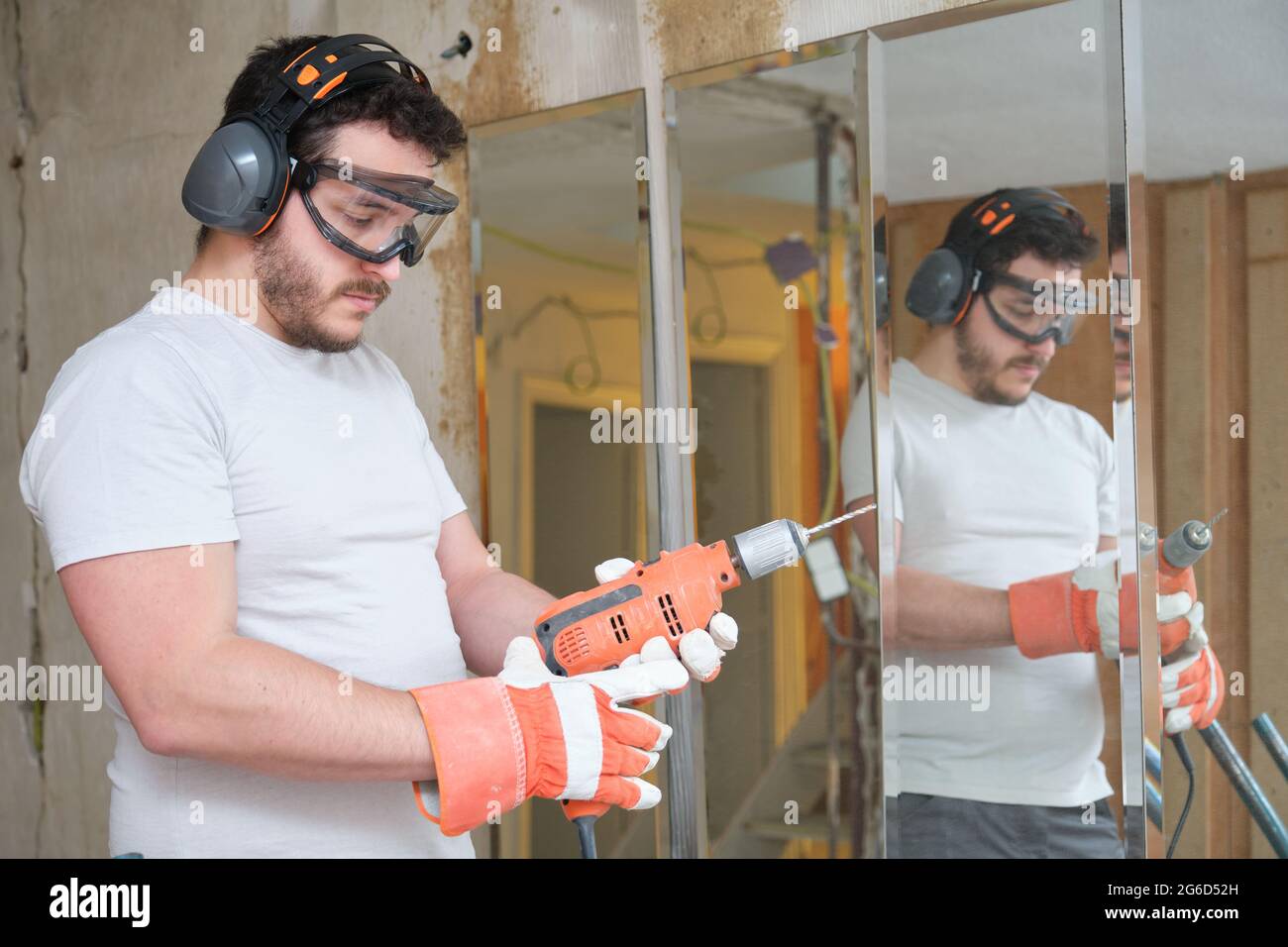 Le constructeur change un foret sur le chantier de construction. Travailleur de la construction portant des gants de sécurité, des lunettes et des couvre-oreilles. Banque D'Images