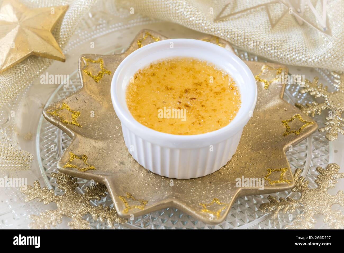 Crème brûlée - dessert traditionnel à la crème vanille française avec sucre caramélisé sur une assiette en forme d'étoile dorée et décoration de noël dorée Banque D'Images