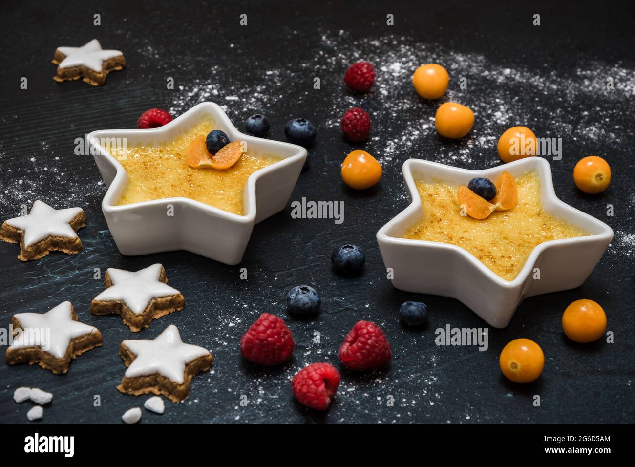 Crème brûlée - dessert traditionnel à la crème vanille française avec sucre caramélisé sur fond noir, servi avec des baies et des biscuits de noël Banque D'Images
