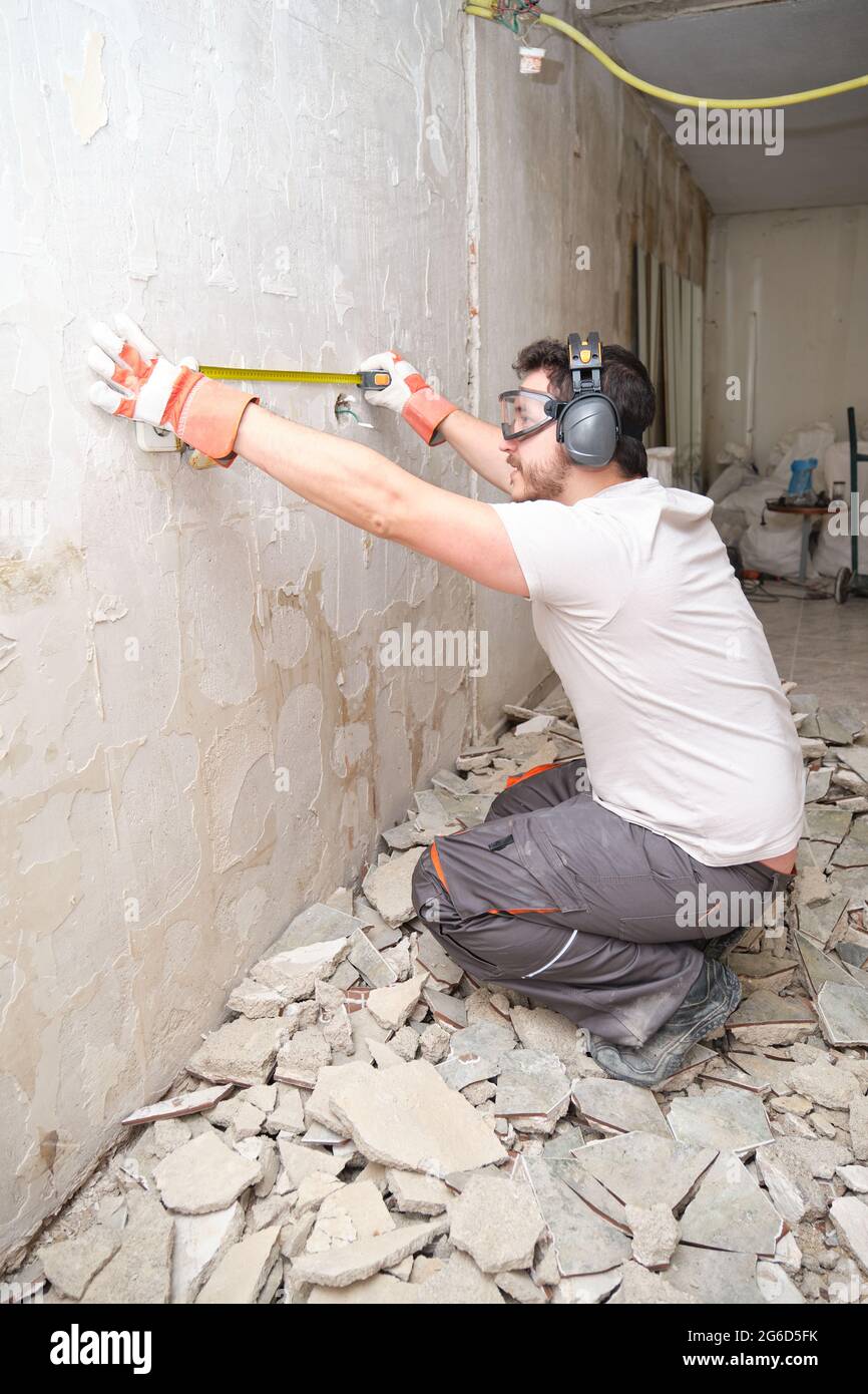 Homme de construction utilisant un ruban de mesure sur le chantier de construction. Travailleur de la construction portant des gants de sécurité, des lunettes et des couvre-oreilles. Banque D'Images