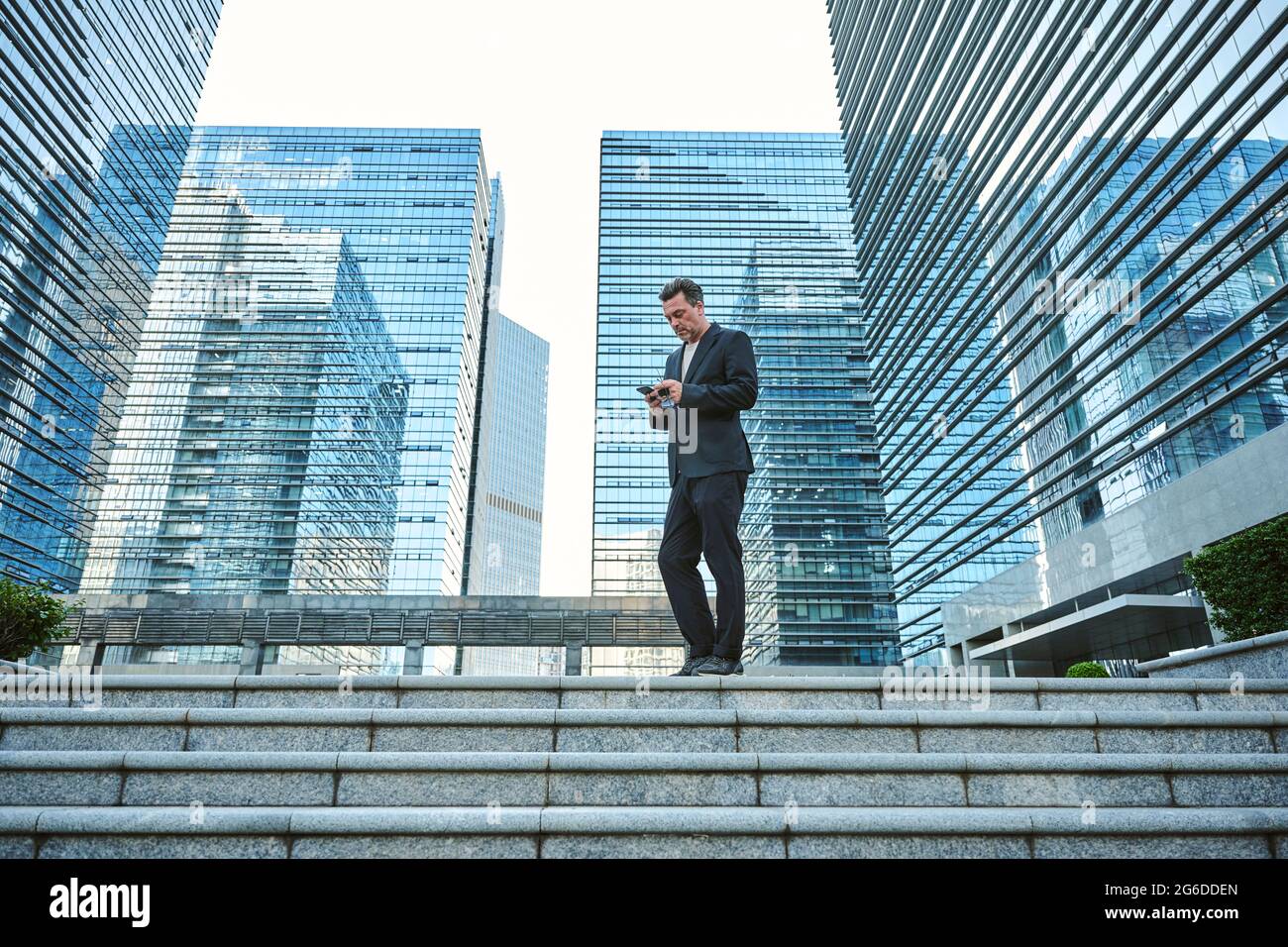 Homme d'affaires qui vérifie son smartphone et qui se promette dans les bâtiments du bureau Banque D'Images