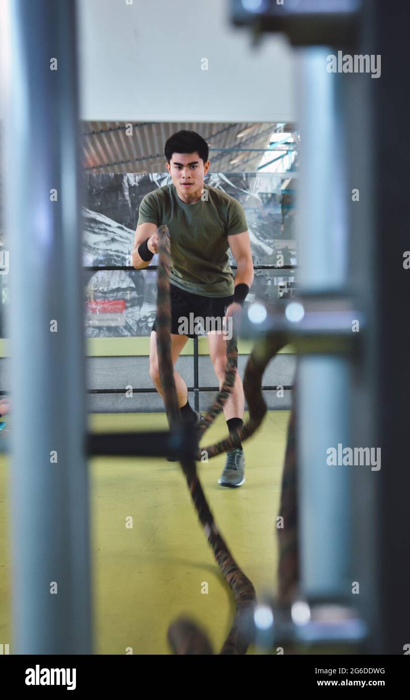 Entraînement d'homme asiatique concentré avec corde de combat dans un gymnase crossfit moderne Banque D'Images