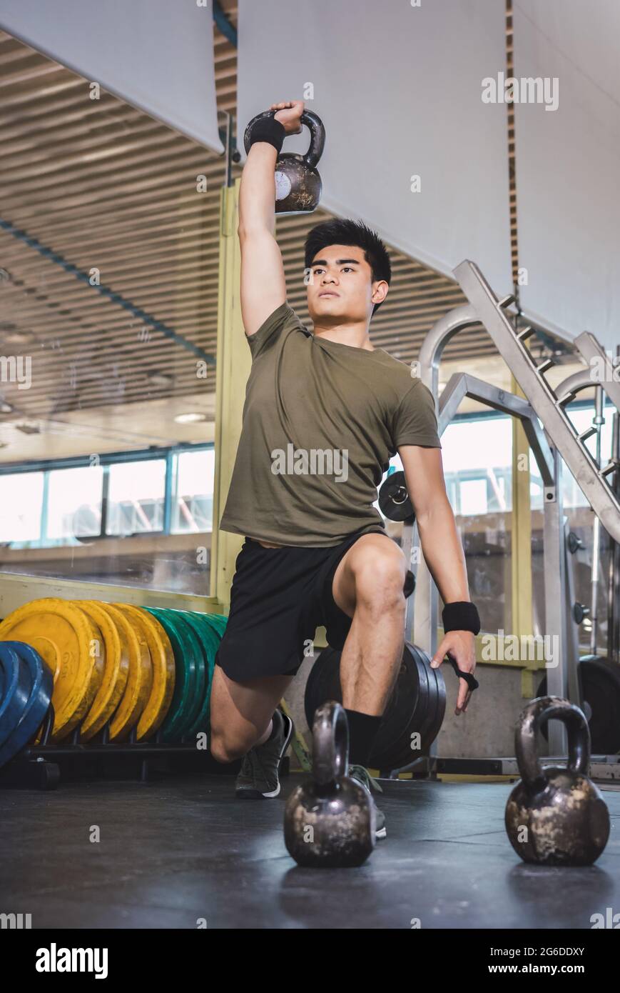 Homme asiatique s'entraîner sur les épaules et les bras avec de lourdes kettlebells dans la salle de gym pendant l'entraînement fonctionnel et regarder loin Banque D'Images