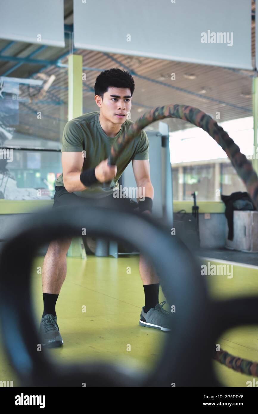 Entraînement d'homme asiatique concentré avec corde de combat dans un gymnase crossfit moderne Banque D'Images