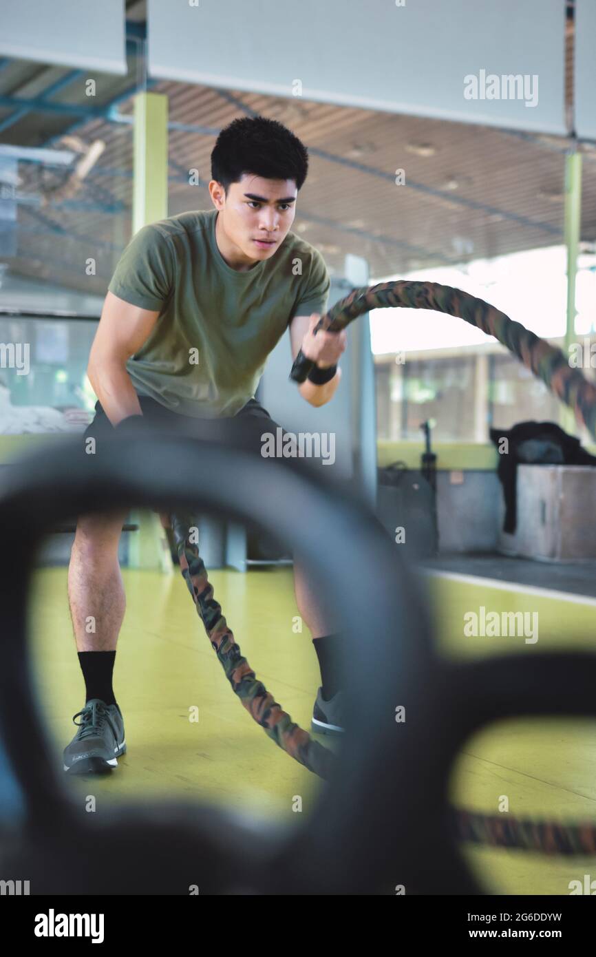 Entraînement d'homme asiatique concentré avec corde de combat dans un gymnase crossfit moderne Banque D'Images