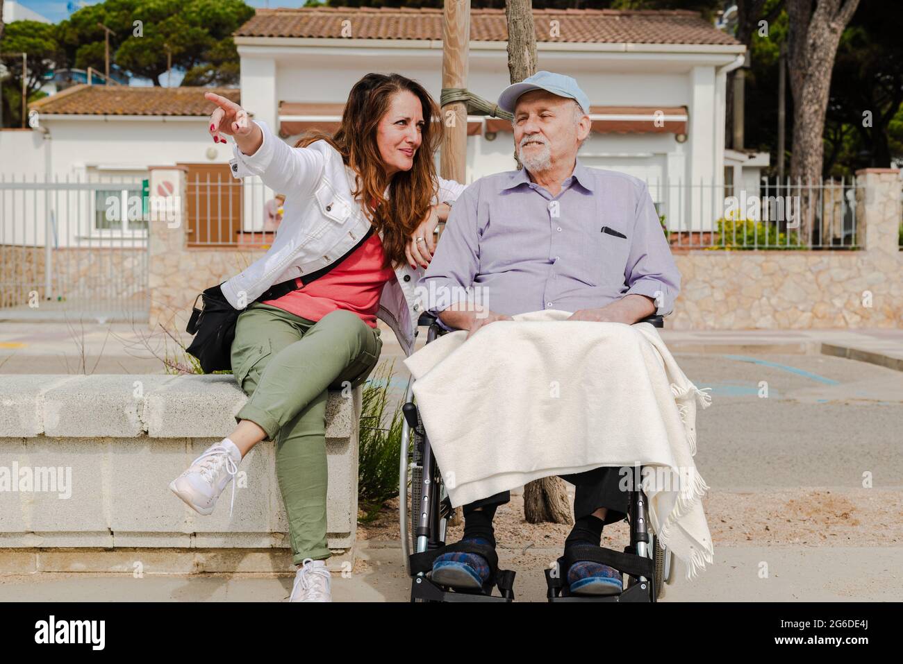 Femme adulte souriante et homme âgé en fauteuil roulant se détendant ensemble en ville par beau temps Banque D'Images