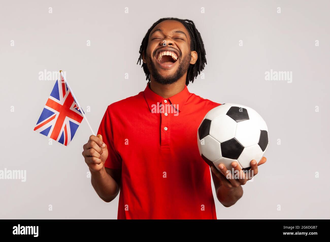 Homme extrêmement heureux avec drapeau britannique et ballon noir et blanc portant le T-shirt de style décontracté rouge, applaudisant pour son équipe préférée, se réjouissant de gagner. IND Banque D'Images