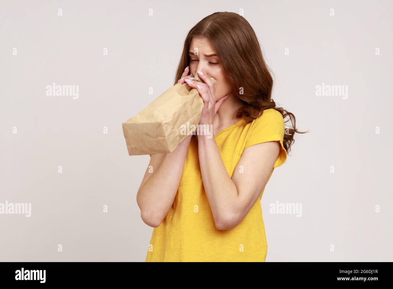 Portrait d'une jeune fille nerveuse qui se sent malade, qui respire dans un  sac en papier pour améliorer le bien-être, surmonte le stress au travail,  porte un T-shirt jaune. IND Photo Stock -